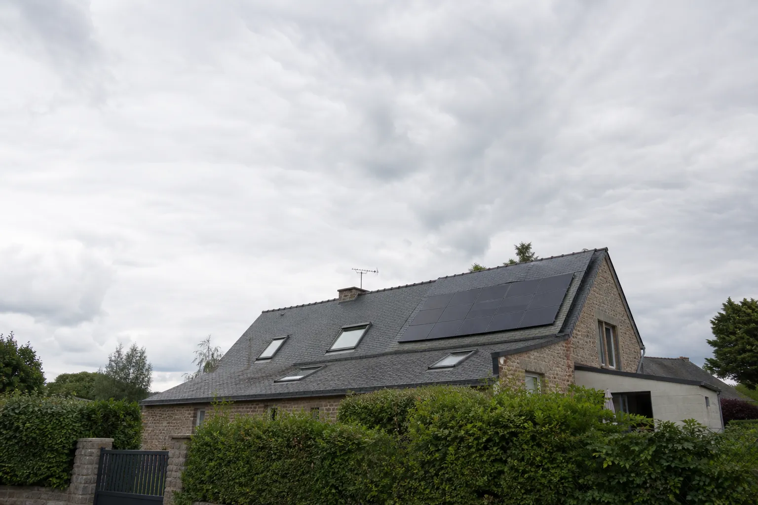 Toiture en ardoise d’une maison bretonne équipée de panneaux solaires, vue extérieure sous un ciel nuageux changeant